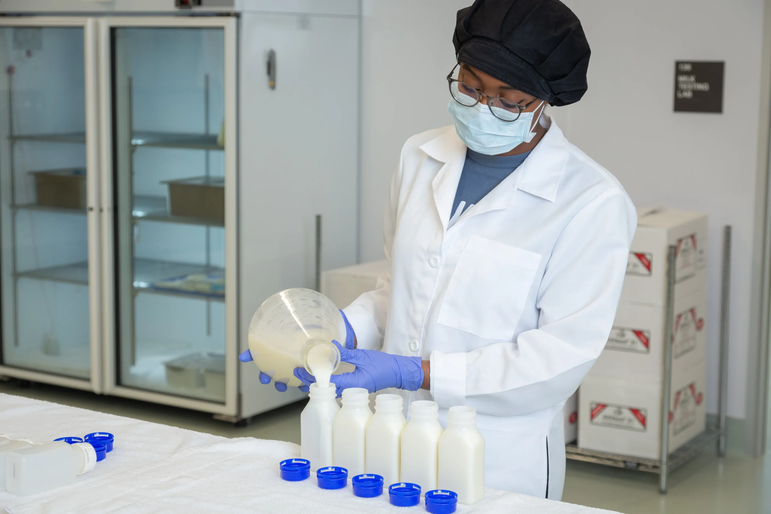 A lab technician wearing protective gear pours human milk into bottles in a milk bank processing room.