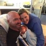 A mother and father smiling while holding their premature baby, who is wrapped in a blanket and connected to medical breathing support in a NICU setting.