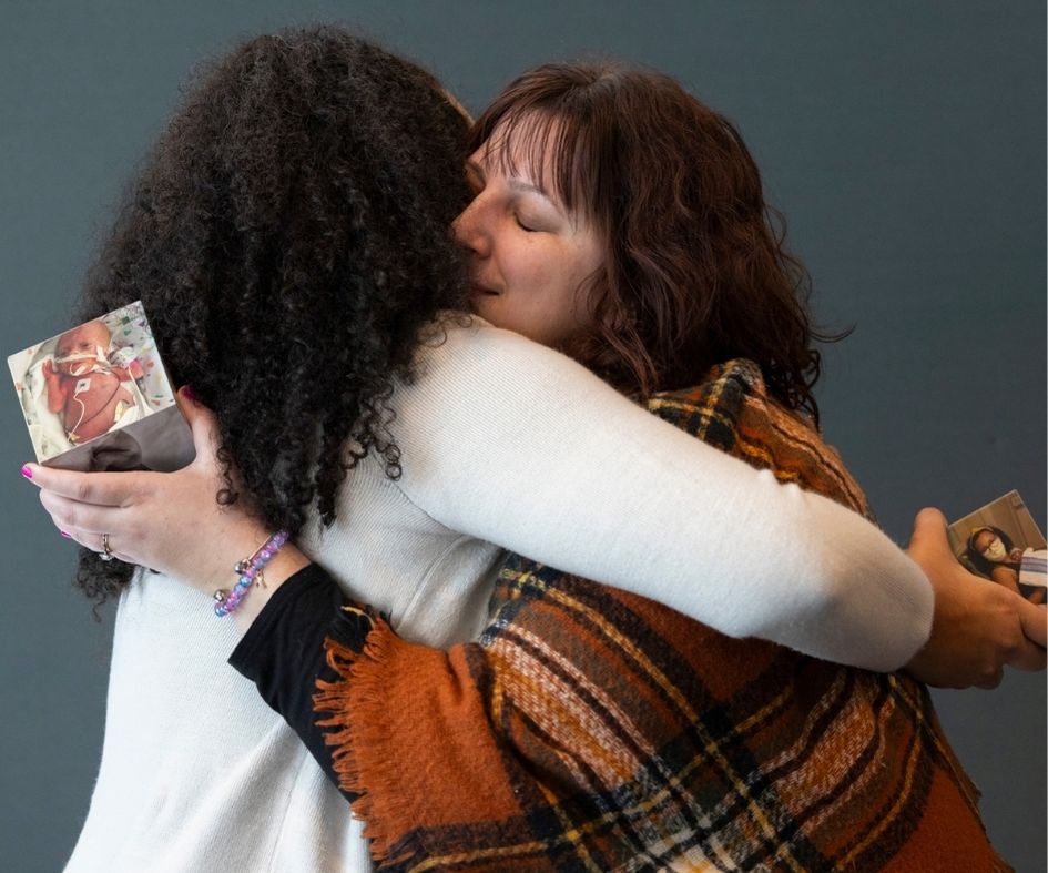 Tabitha and Cassey hugging while holding pictures of their daughters who tragically passed away
